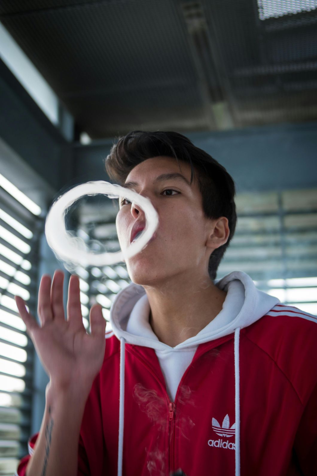 Young man exhaling a vape cloud and blowing smoke rings, showcasing vaping skills near a vape shop in Houston.
