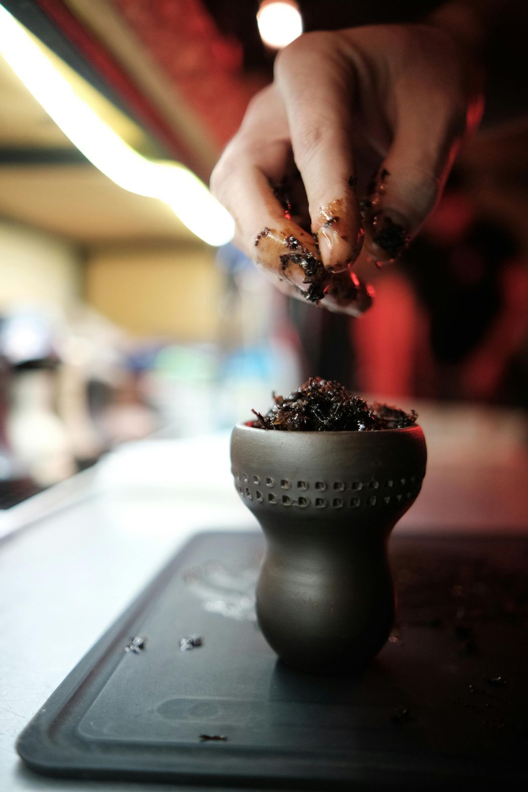Person filling a hookah bowl with tobacco at a tobacco shop in Houston, preparing for use.