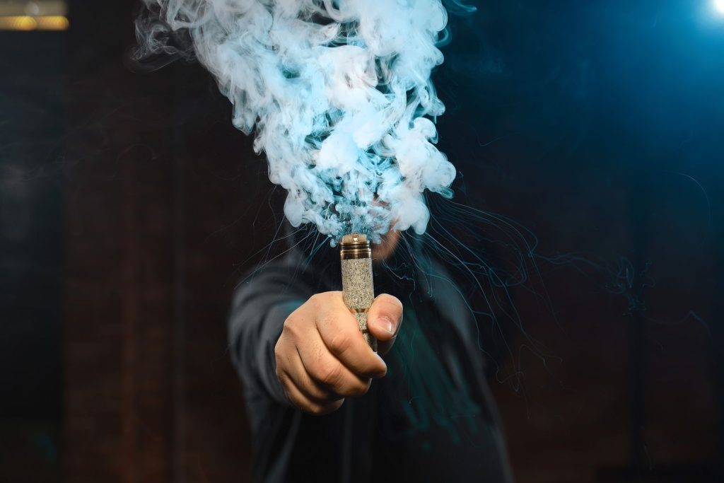 Hand holding a premium vape pen exhaling dense blue vapor in a dynamic display, perfect for exploring options at your local cigarette shop in Houston.