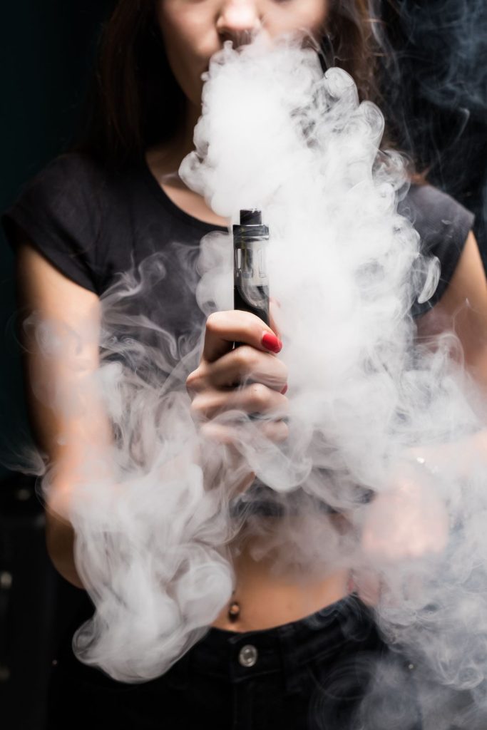 Woman enjoying a smooth vape session with thick white clouds, highlighting the relaxing experience available at top cigarette shops in Houston.