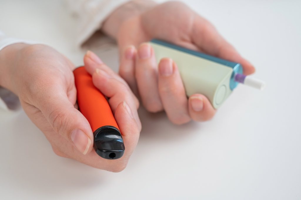 Hands holding colorful vape devices, showcasing trendy options available at a vibrant head shop in Houston.