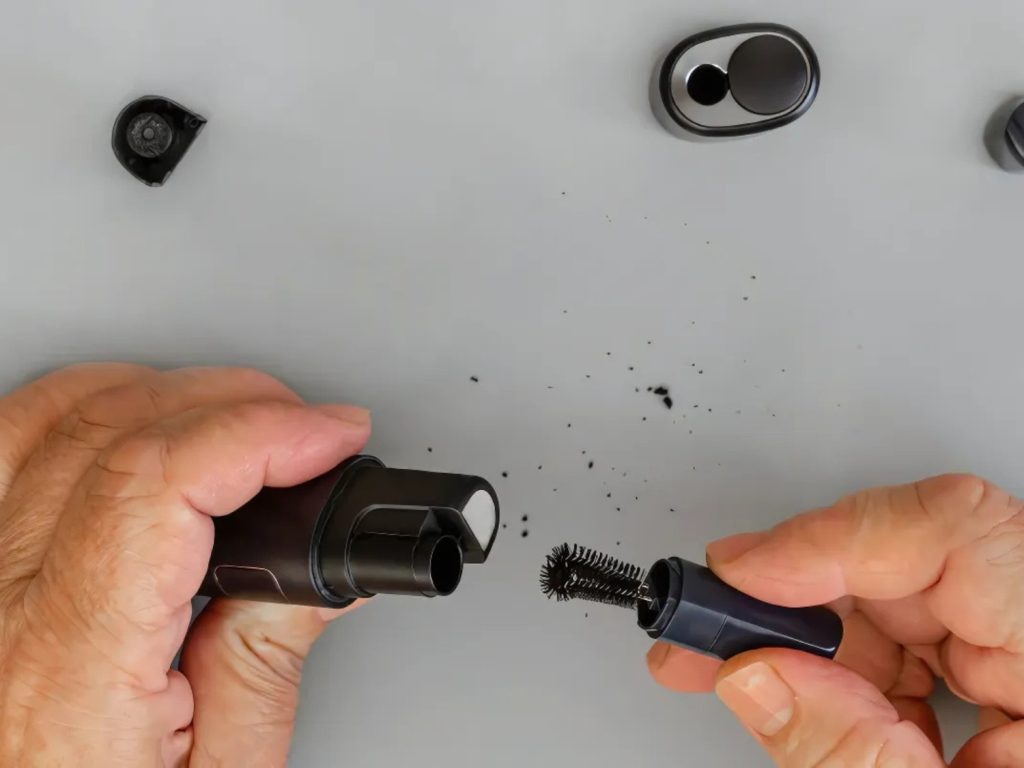 Hands cleaning a vape device with a brush, offered by a vape shop Houston.