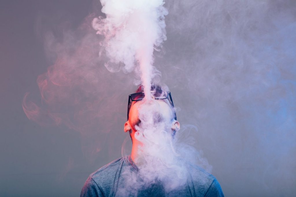 Man exhaling thick vape clouds with a stylish vape device, showcasing the trendy vibe of a head shop in Houston.