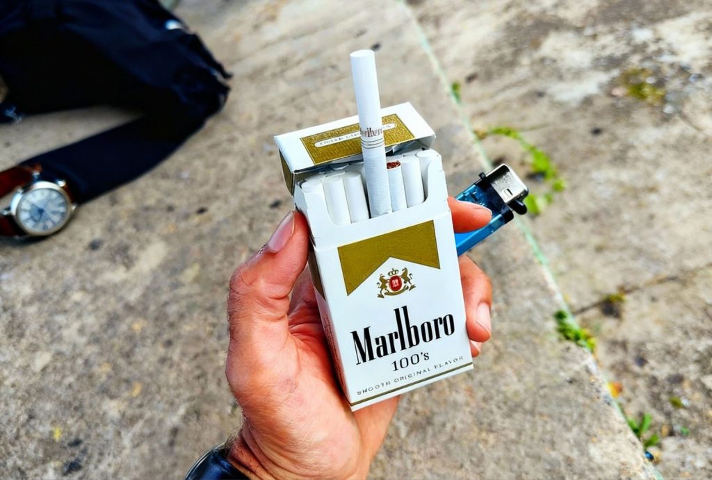 Person holding Marlboro 100’s pack with lighter, ready to go at cigarette shop Houston.