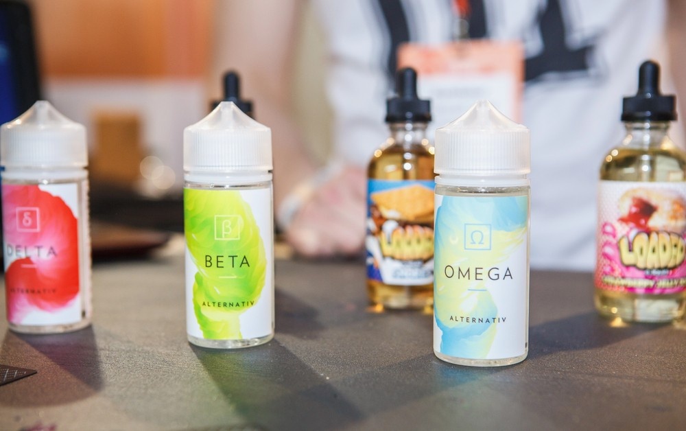 Row of premium e-liquid bottles labeled Delta, Beta, and Omega in various colors, showcased at our alternative smoke shop Houston for high-quality alternatives.