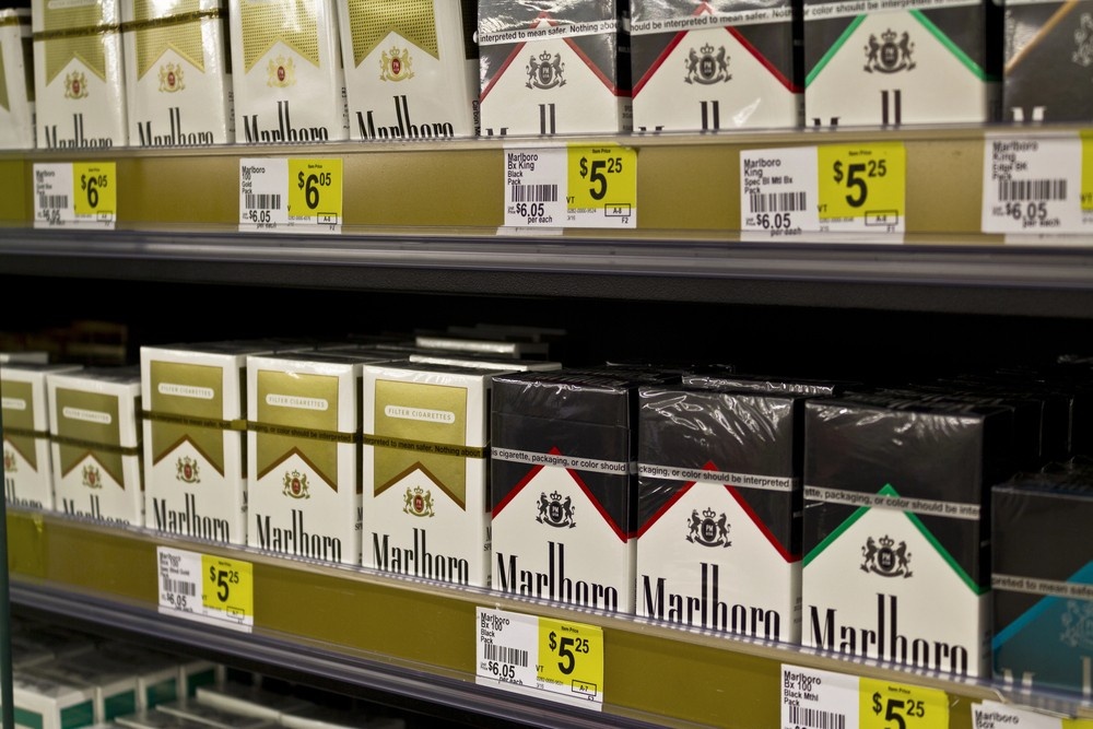 Rows of Marlboro cigarette packs neatly arranged on tobacco shop shelf with price tags, showing various styles and packaging options for customers.