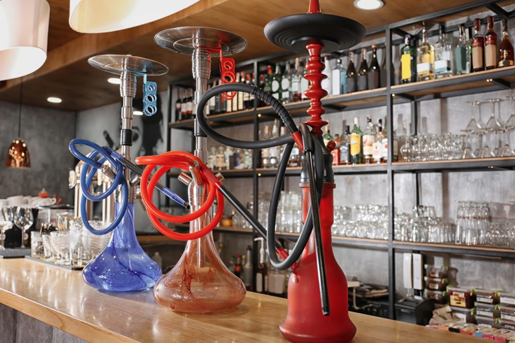 Three stylish hookahs in blue, red, and clear designs with hoses displayed on a wooden bar at a top-rated hookah shop in Houston lounge.