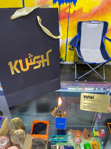 A glass display counter at a head shop in Houston featuring Kush branded shopping bags, a blue torch lighter, and various glass pipes