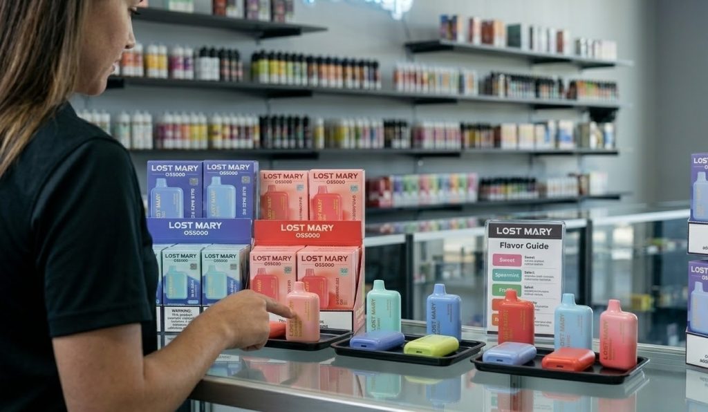 A Houston vape shop employee points to a clean display of Lost Mary OS5000 flavors Cherry Peach Lemonade and Blue Razz Ice.