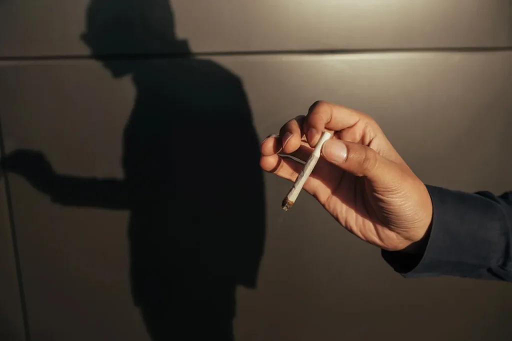 A hand holds a lit joint with a smoker's silhouette, displaying a product often used with rolling papers houston.