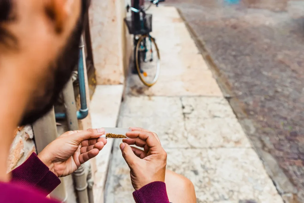 A man sitting outdoors rolls a cigarette using premium loose tobacco and one of the quality rolling papers houston has.