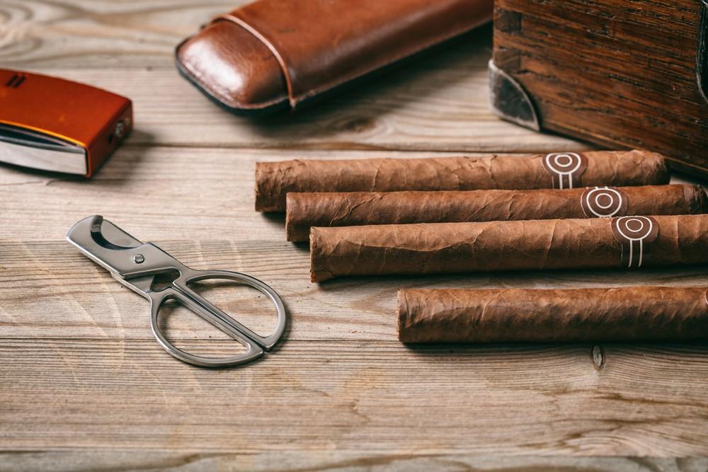 Multiple branded cigars and a classic scissor cutter on a wooden surface, highlighting a premium choice in smoke accessories Houston.