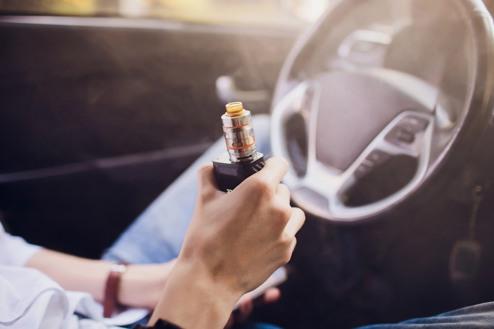 Hand holding a modern sub ohm tank vape kit from a top vape store Houston while sitting at the steering wheel.