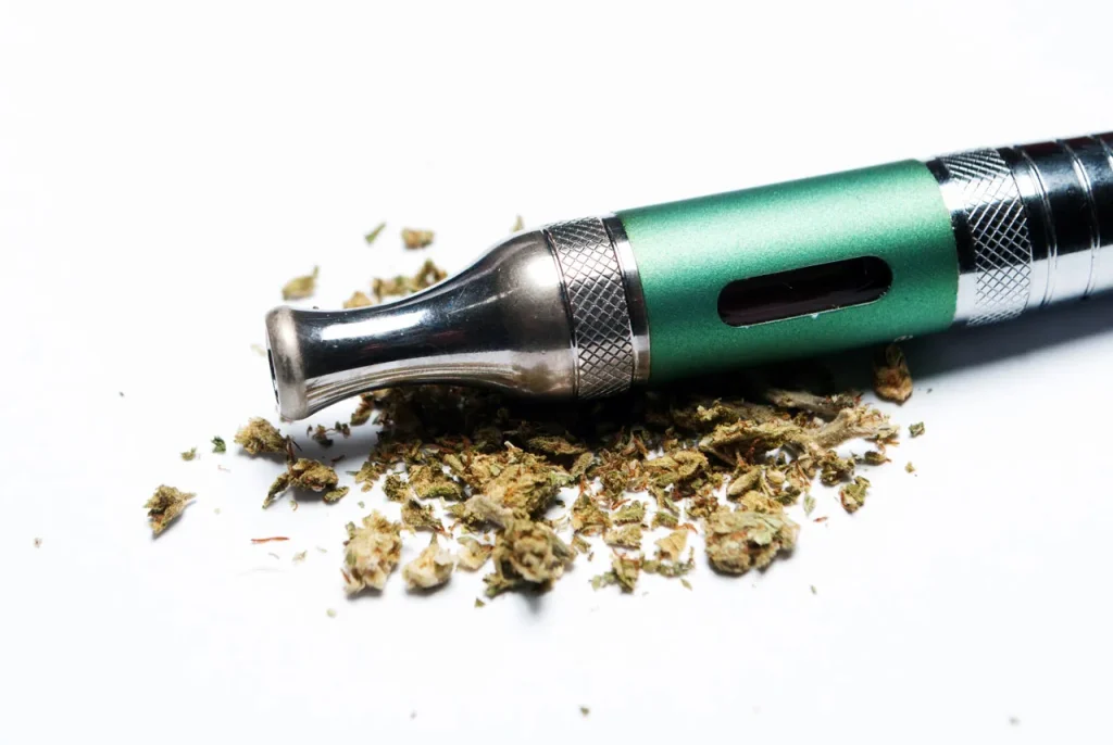 Green dry herb vape pen resting on ground cannabis, perfect for premium herbal vaporizers Houston enthusiasts.