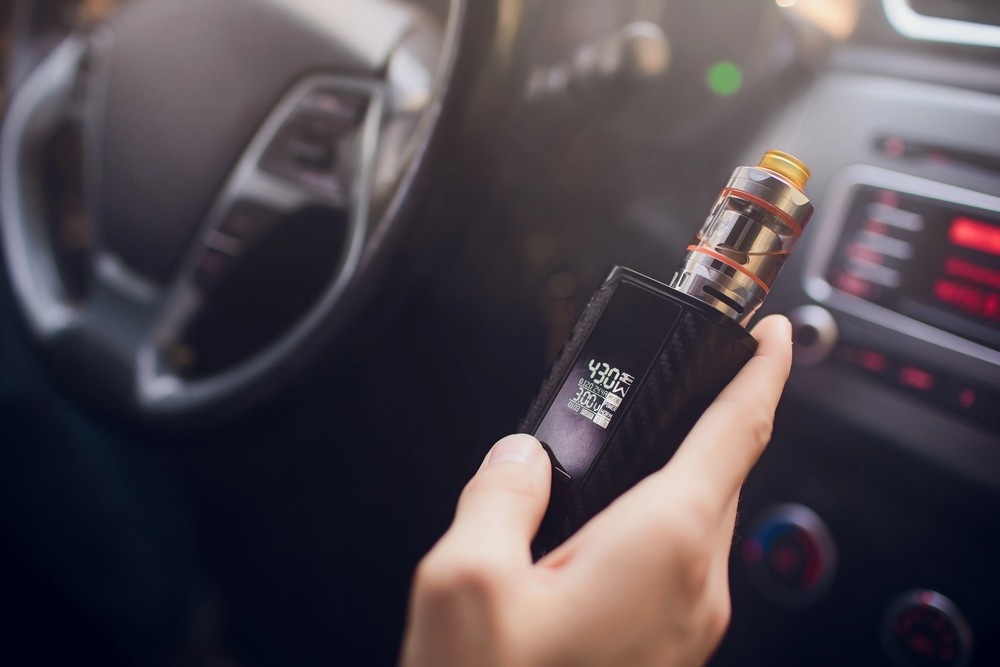 Premium box mod mod from a vape store Houston held by a driver showing digital display settings inside a car.