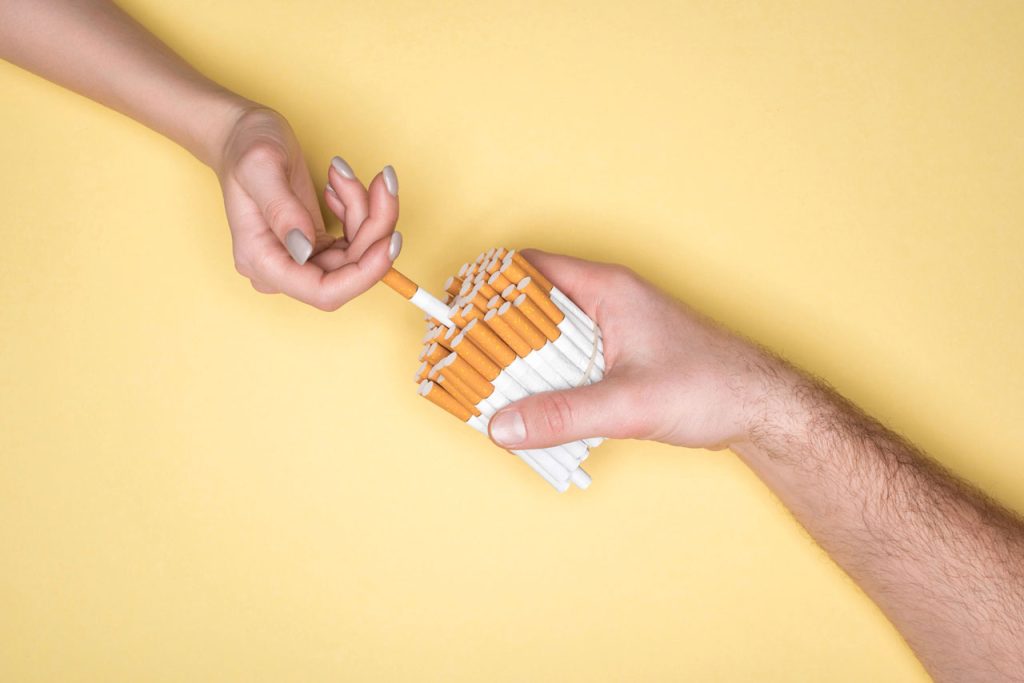 Two hands exchanging a cigarette from a large, rubber-banded bundle. Stock for a top cigarette shop Houston blog.