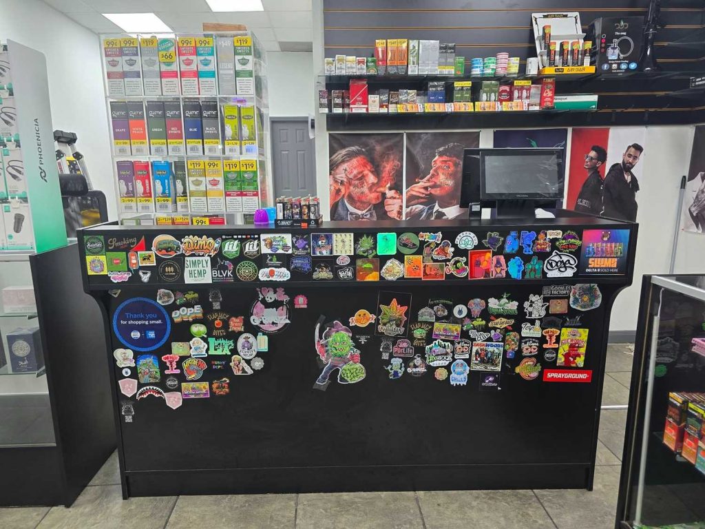 Vibrant interior of a cigarette shop in Houston with sticker-adorned counter, shelves of tobacco products, and eye-catching posters for vaping enthusiasts.
