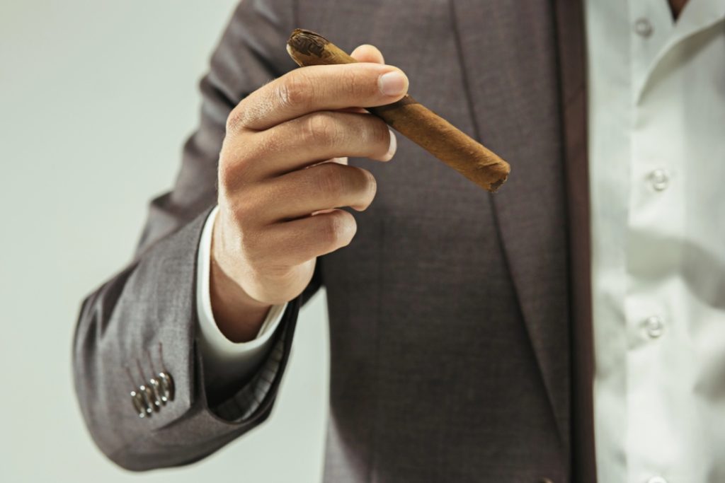 A close-up of a hand in a tailored suit jacket holding a hand-rolled cigar from a luxury cigar shop houston.