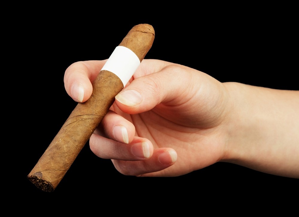 Hand holds a premium cigar with a blank white band against a black background. Discover quality at our cigar shop houston.