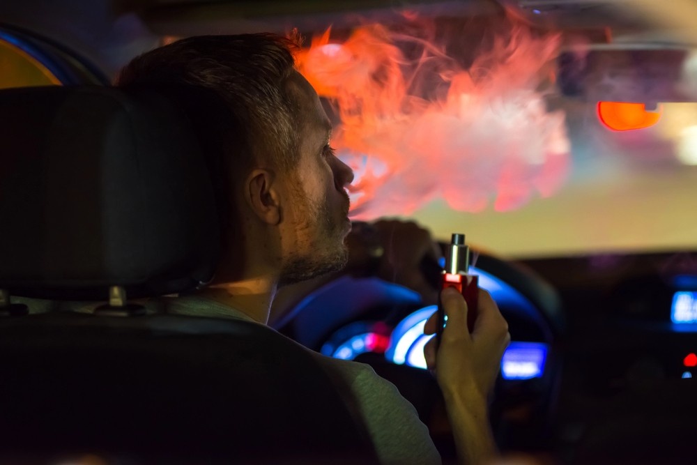 Man buying from a vape store Houston exhales a large vapor cloud while sitting inside his car at night.