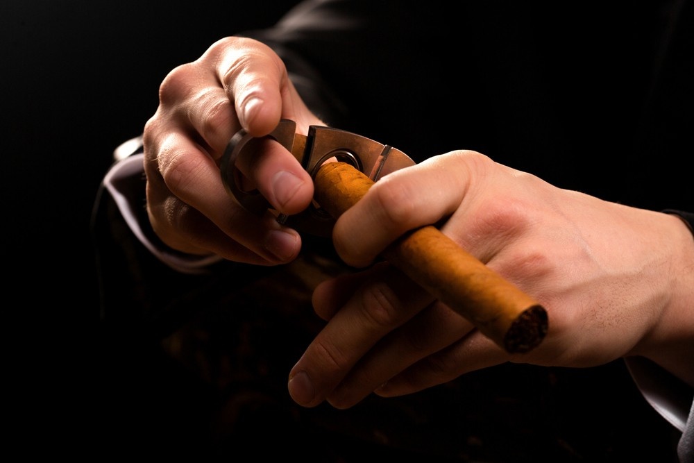 A man in a suit cutting a cigar with a precision tool, a key item among smoke accessories Houston shops.